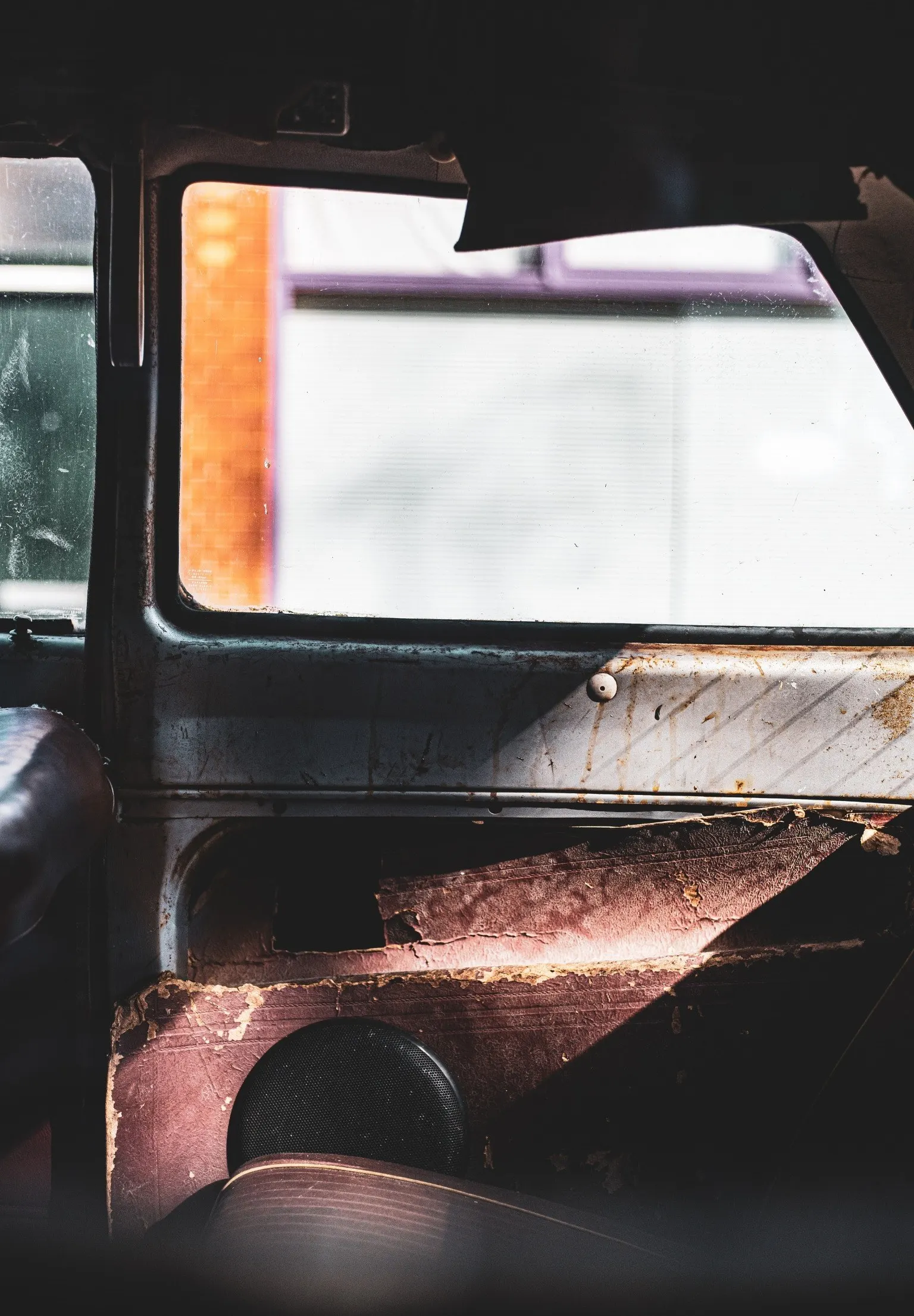 Doorkijk door het raam van een oude auto, met een verroest interieur en een strook zonlicht