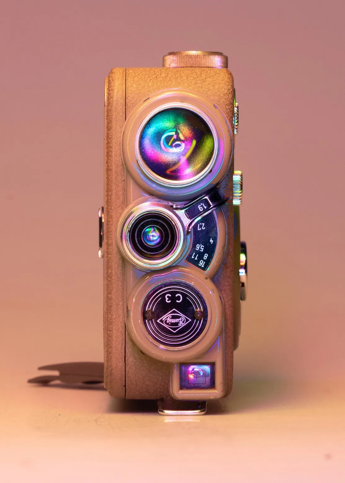 Oude filmcamera met drie lenzen in roze en paars licht, op een pastelkleurige achtergrond