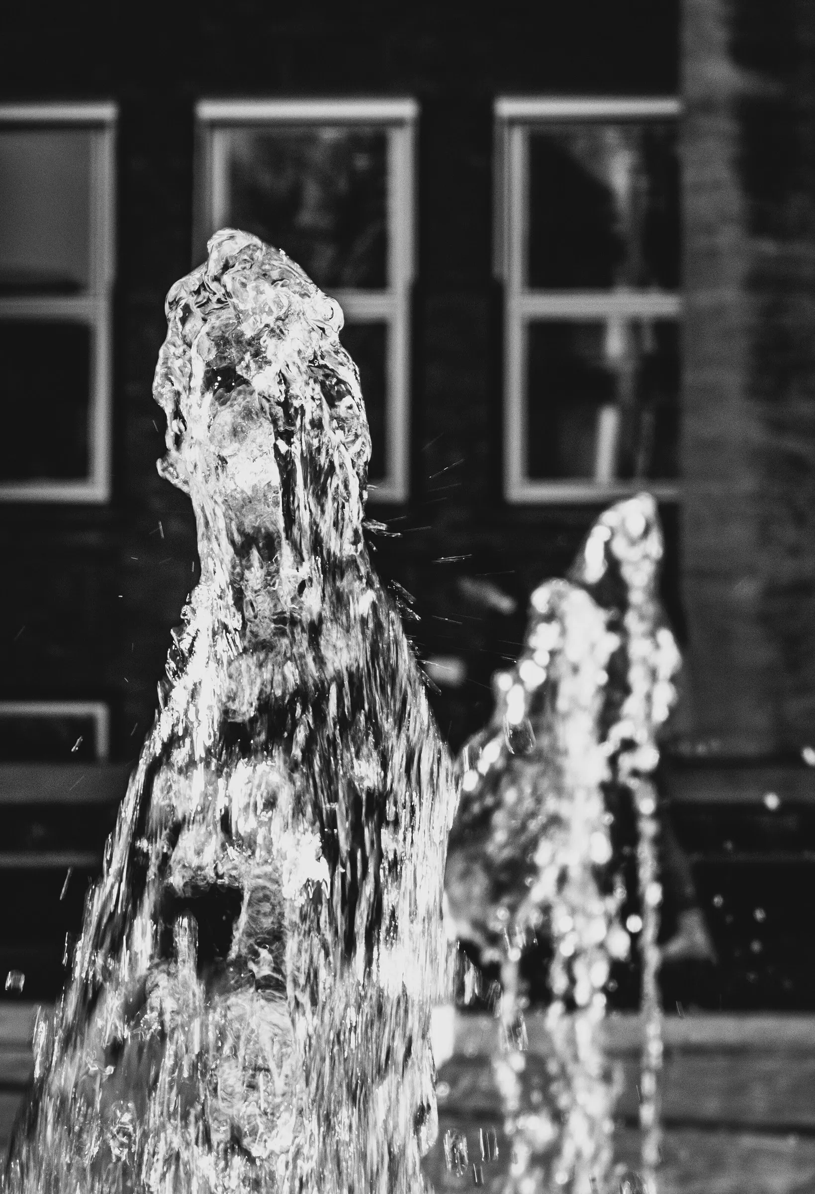 Zwart-witfoto van opspattend water uit een fontein voor een gevel met ramen