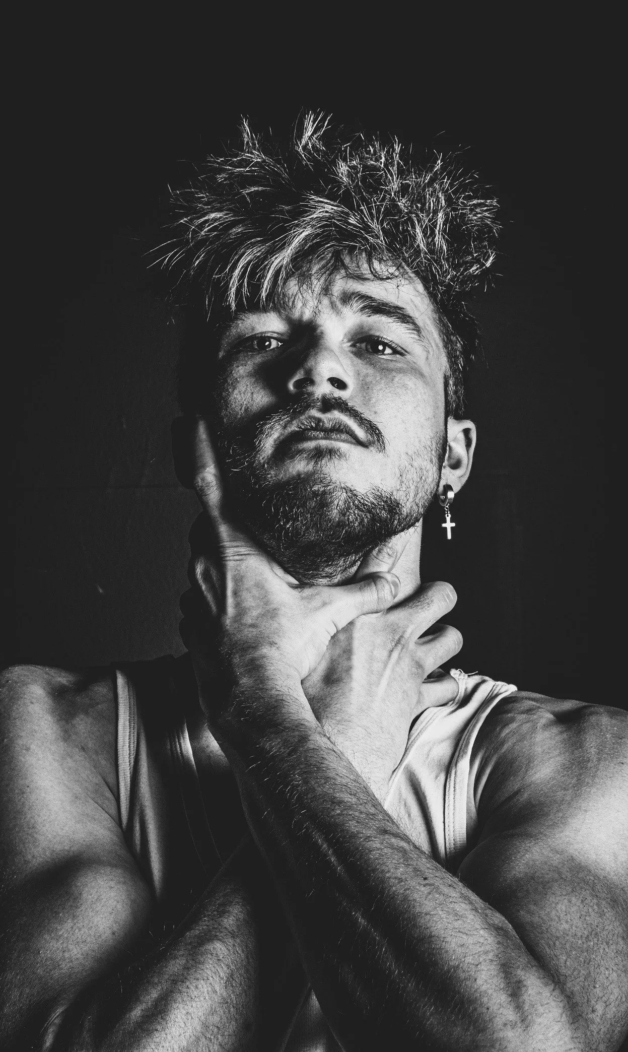 Zwart-witportret van een man met warrig haar en baard, ogen half dicht, zijn hand tegen zijn keel, tegen een donkere achtergrond